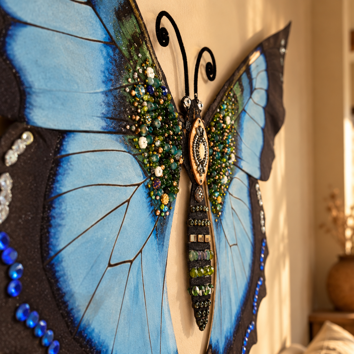 A large decorative butterfly wall hanging with bright blue wings, black outlines, and dense bead and sequin embellishments, shown mounted on a beige wall in a real interior setting.